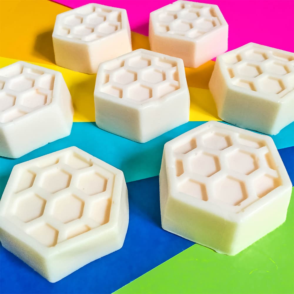 Our homemade honey goats milk soap bars sitting on a colorful rainbow background