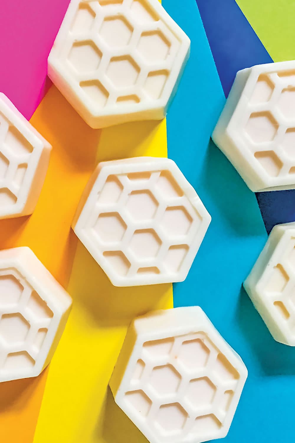 Our DIY honey goats milk soap bars sitting on a colorful rainbow background