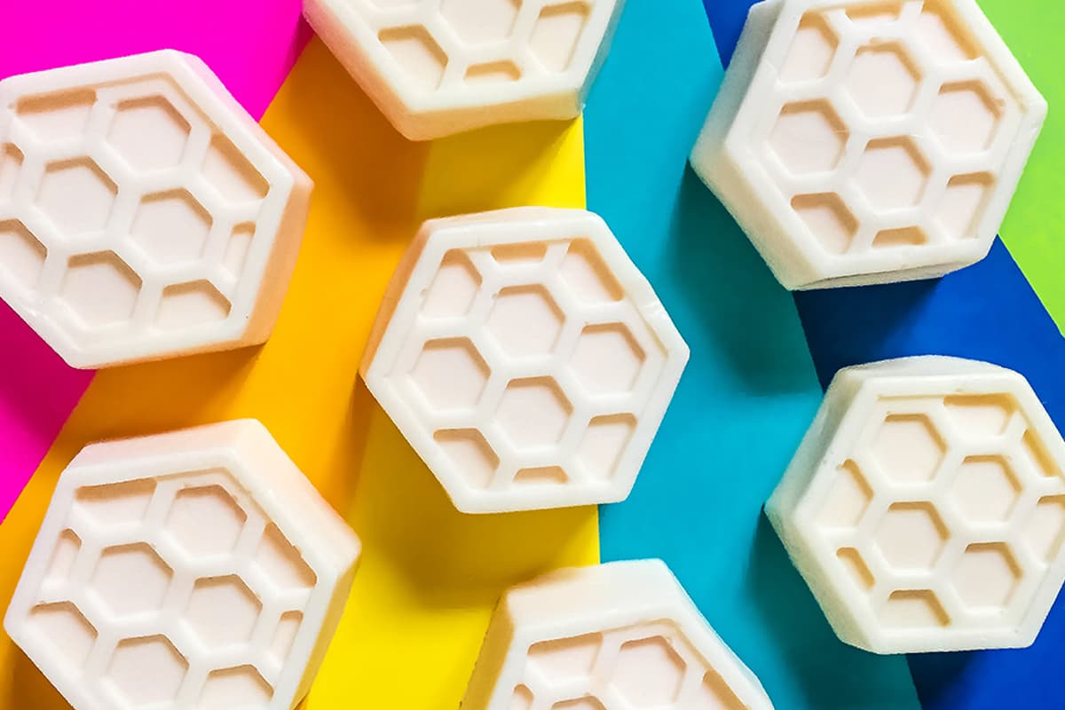 Our DIY honey goats milk soap bars sitting on a colorful rainbow background