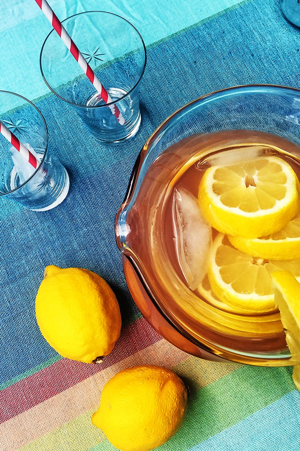 A pitcher of homemade lavender lemonade sitting next to lemons and empty glasses