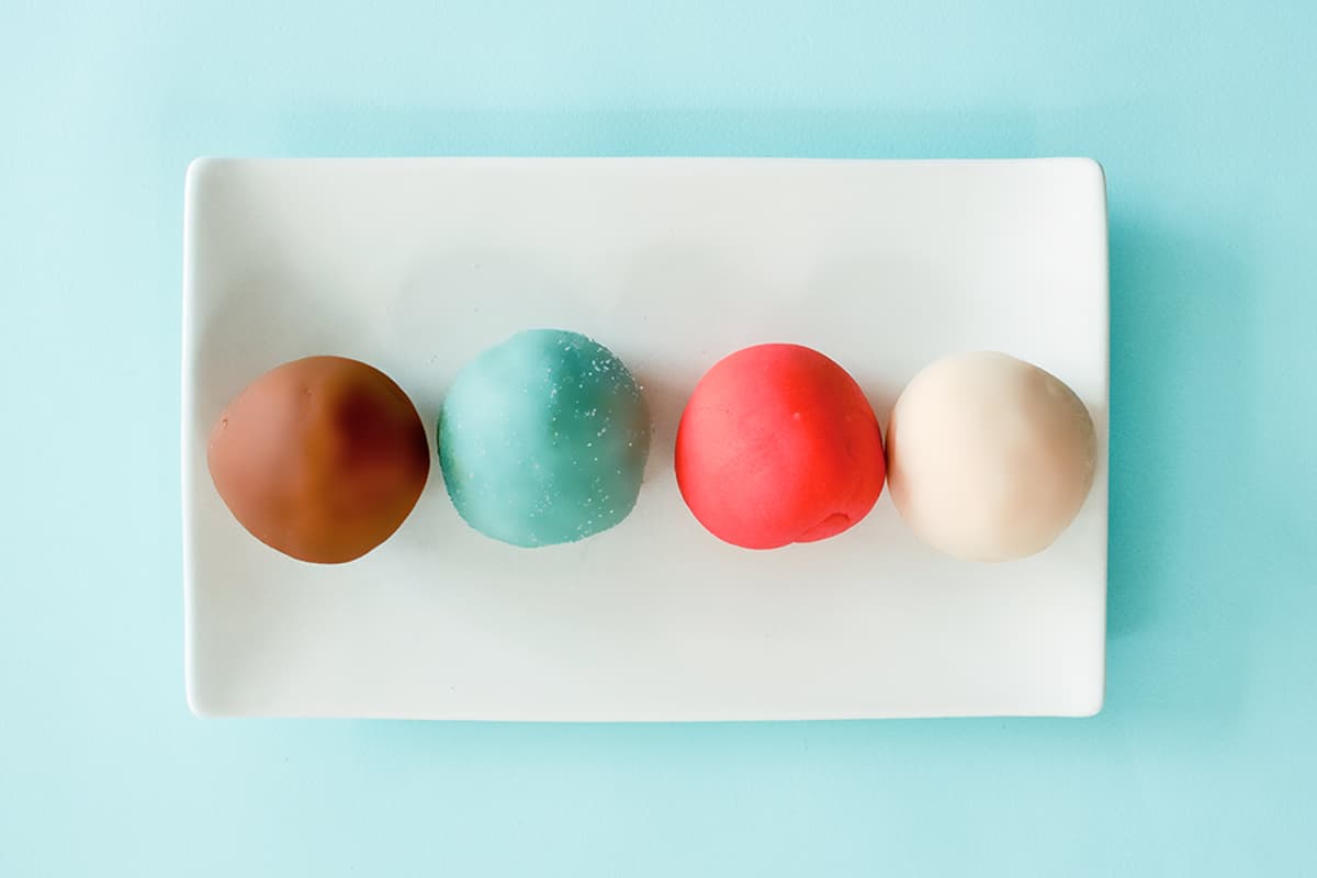 Balls of our DIY winter play dough scented with gingerbread peppermint, sugar cookie, and wintergreen laying on a white plate against a light blue background