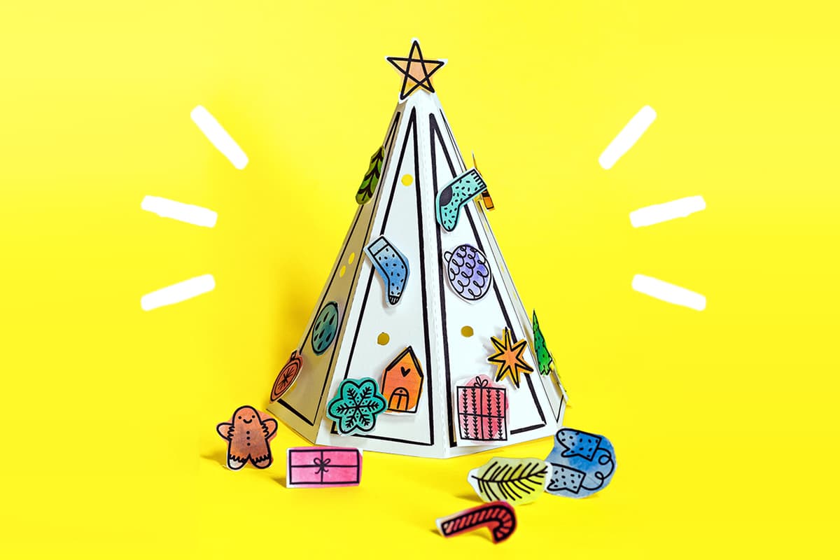 Our DIY paper Christmas tree kids craft sitting against a yellow background surrounded by paper ornaments