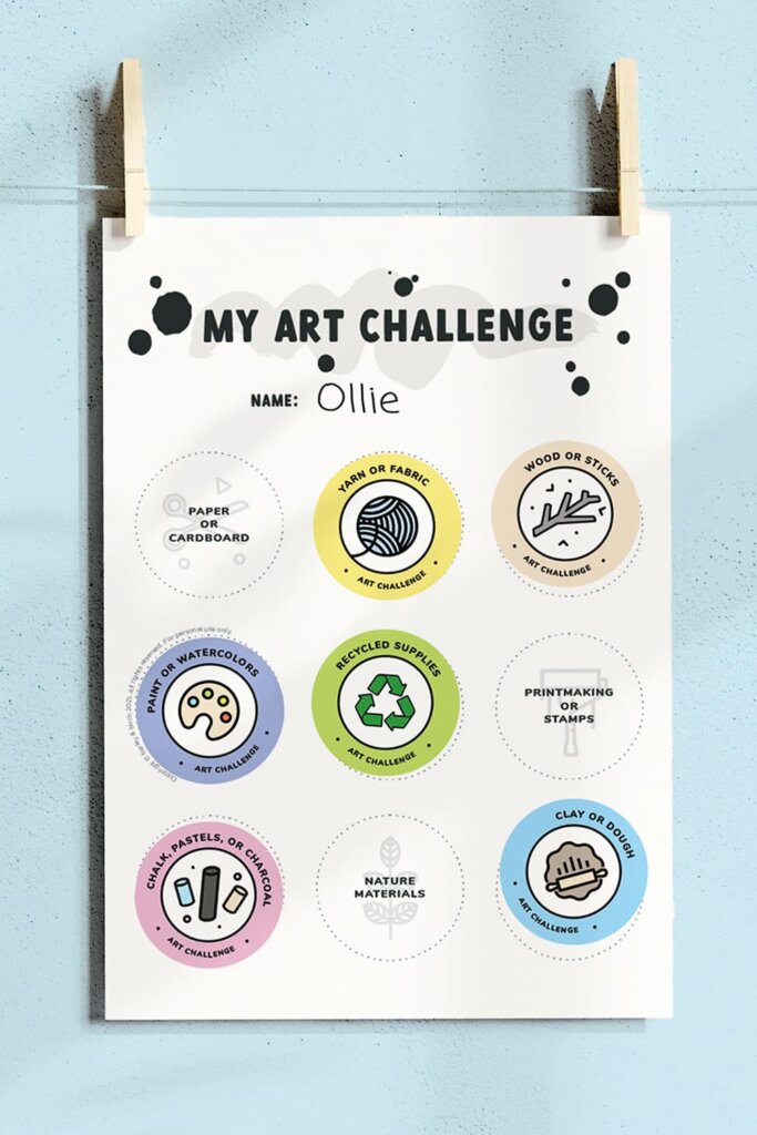 Our printable kids art challenge hanging in front of a blue wall with clothespins
