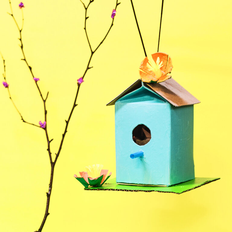 Our recycled juice carton birdhouse decorated with egg carton flowers hanging from a small branch.