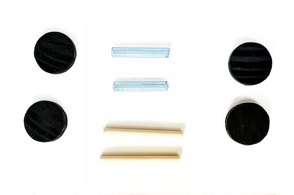 Wood wheels, pieces of drinking straws, and craft dowels sitting on a white background to be assembled into wheels