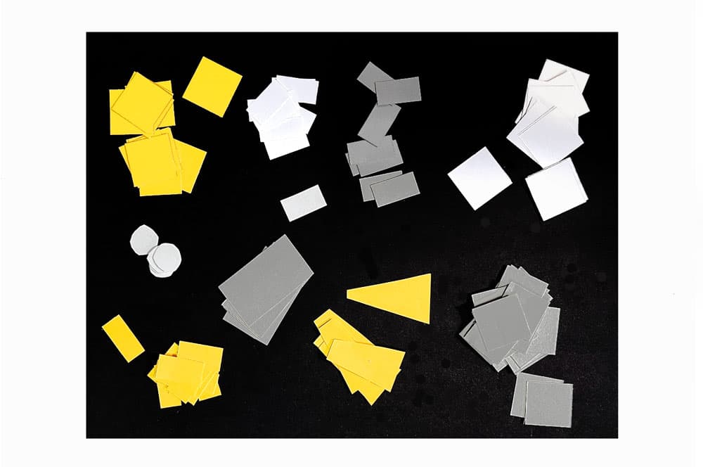 Small yellow, white and gray shapes cut of of construction paper laying on a black background