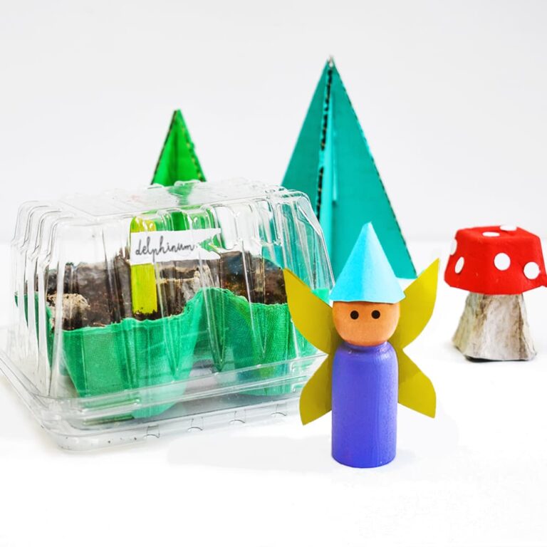 Our DIY fairy greenhouse egg carton seed starter sitting next to cardboard pine trees, an egg carton mushroom, and a fairy peg doll