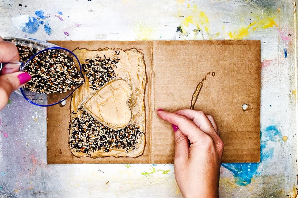 Sprinkling bird seed on cardboard to make a cardboard bird feeder