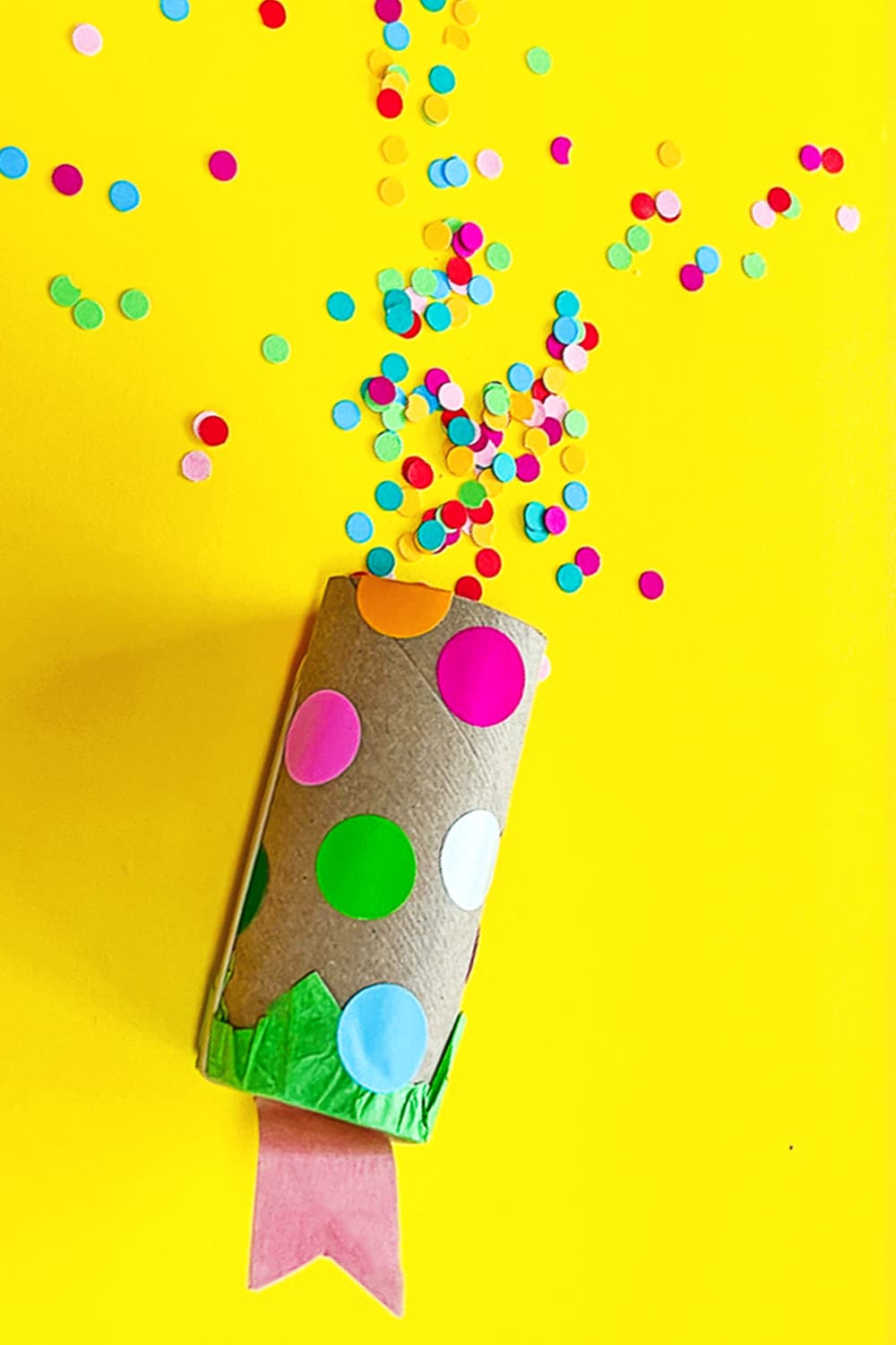 Our DIY confetti popper craft sitting on a yellow background sprinkled with confetti