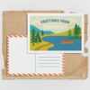 Illustrated DIY postcard for kids featuring a lake landscape. The front includes a “Greetings From” banner with space to write a location. The back shows a traditional postcard layout with an address area and striped border.