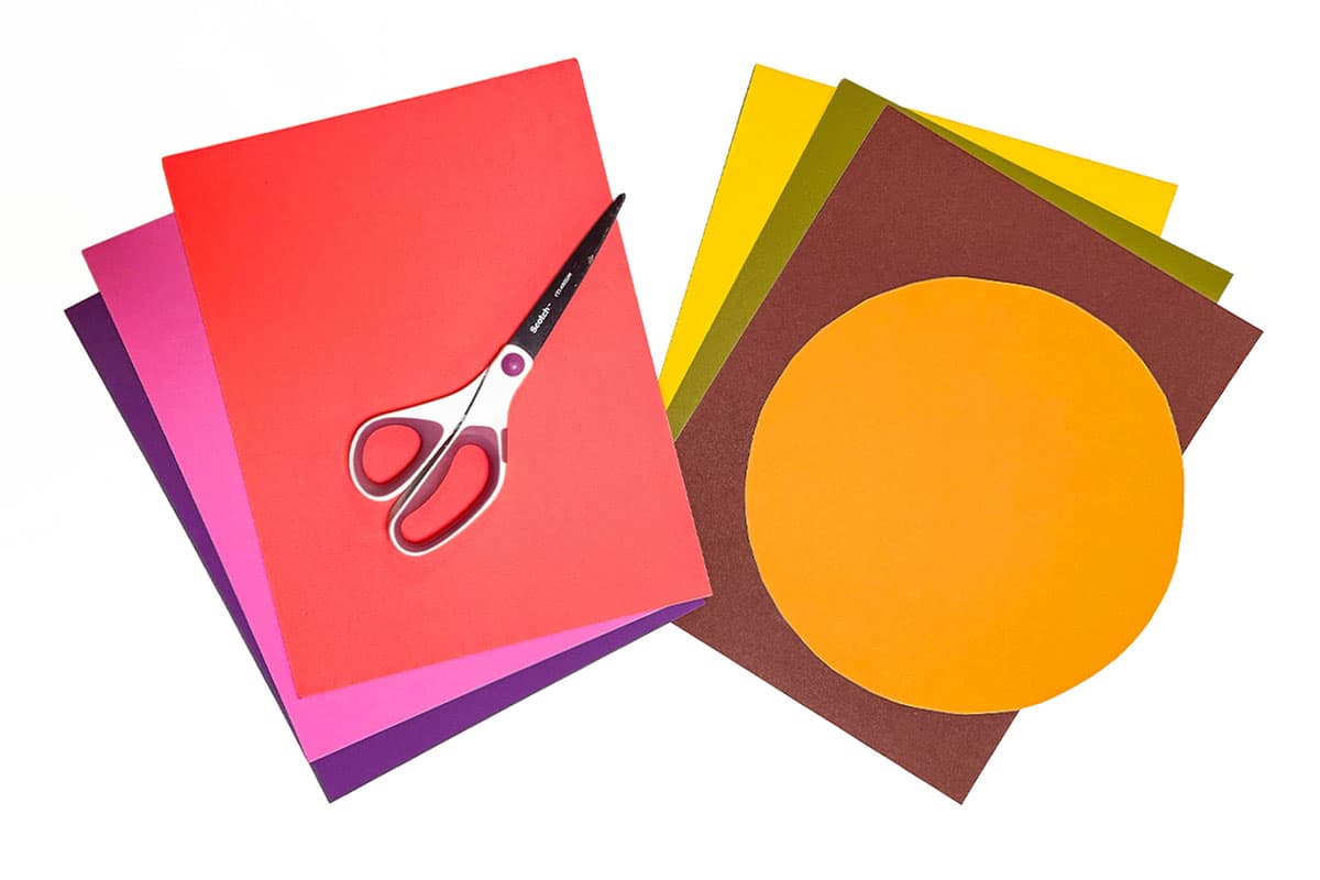 A process photo showing colorful construction paper stacks sitting on a white background with a pair of scissors