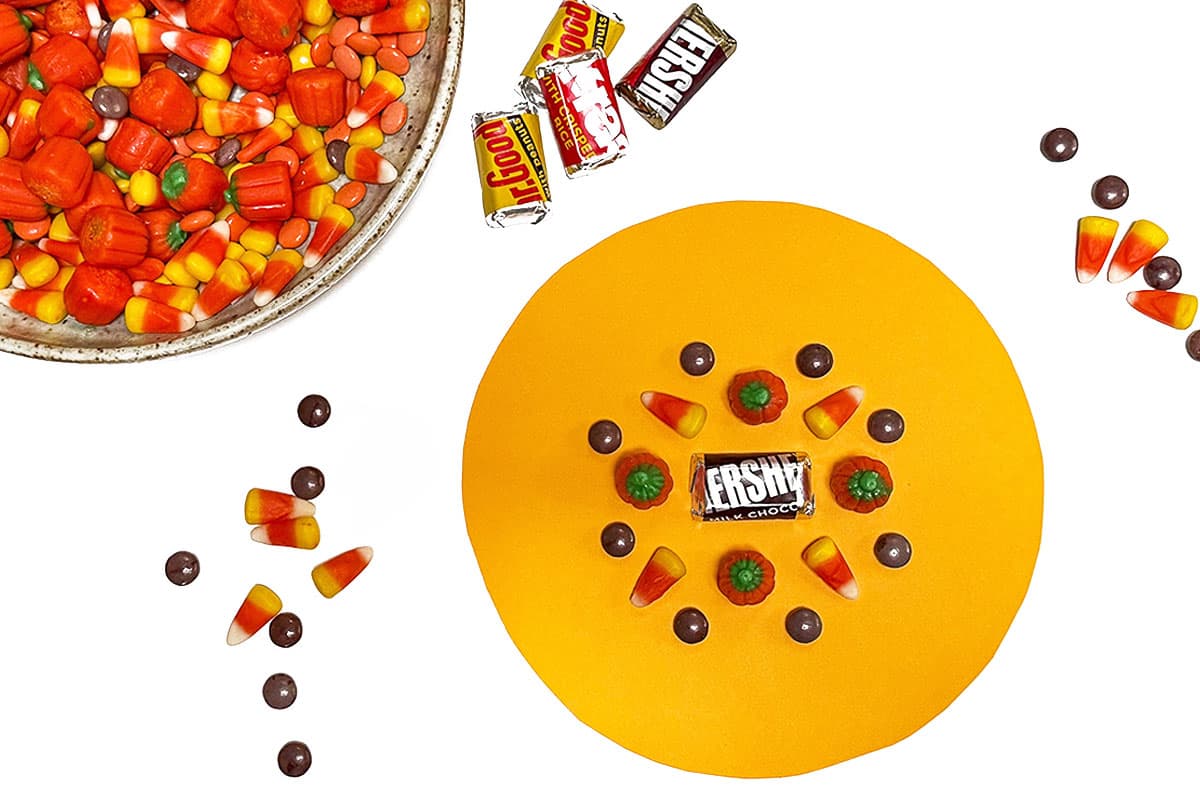 A process photo showing the beginning of a candy mandala next to a bowl of Halloween candy sitting on a white background