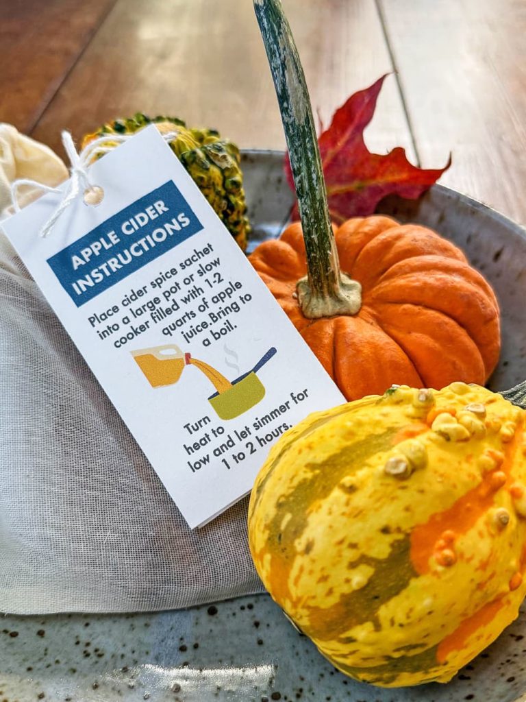 A piece of pottery sitting on a wood table filled with an arrangement of gourds and kid-made apple cider spice sachets