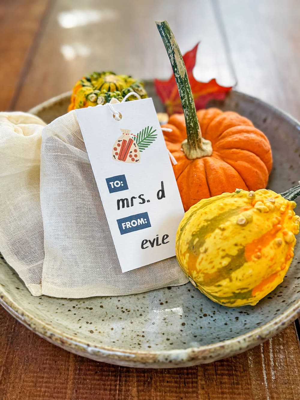 A piece of pottery sitting on a wood table filled with an arrangement of gourds and handmade mulling spice bags