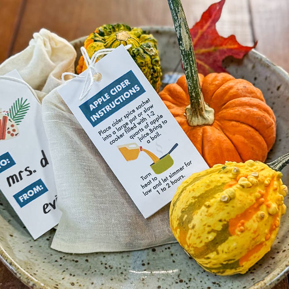 A piece of pottery sitting on a wood table filled with an arrangement of gourds and handmade mulling spice favors