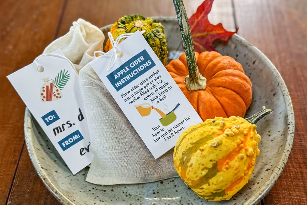A piece of pottery sitting on a wood table filled with an arrangement of gourds and handmade cider sachets