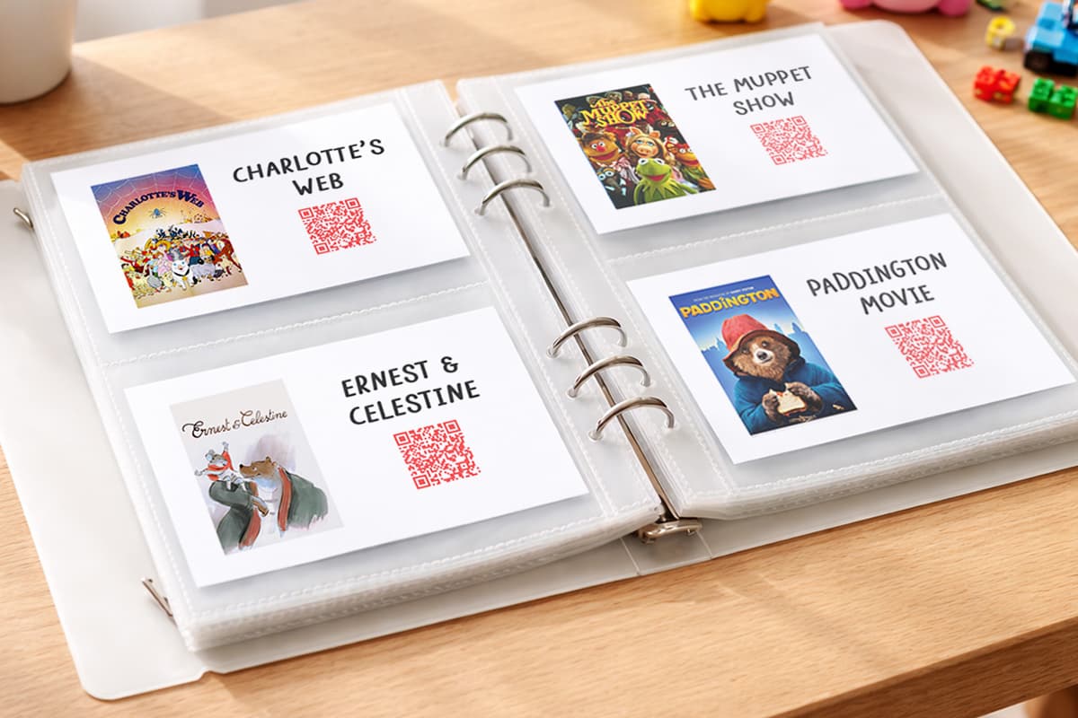 A binder with cards that have approved childrens streaming movies and titles with a QR code. The binder is sitting on a table next to childrens toys.