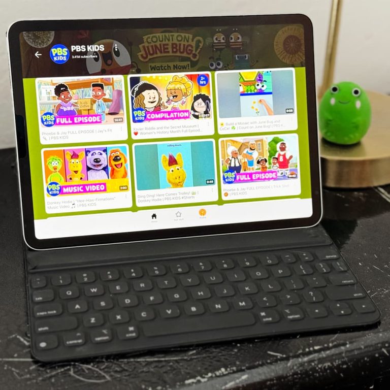 A tablet sitting on a desk next to a lamp and children's toys. The YouTube Kids app is on the screen of the tablet.